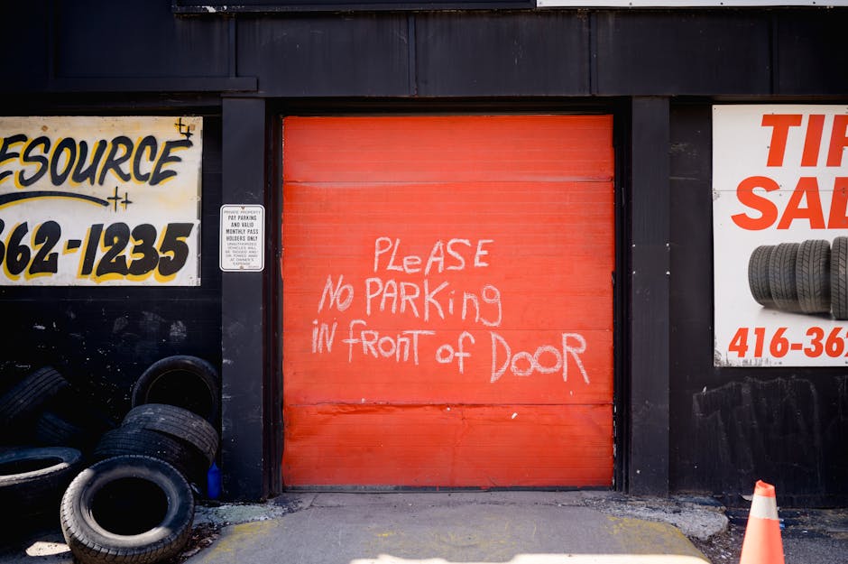 Red garage door with handwritten no parking sign surrounded by tire shop advertisements.